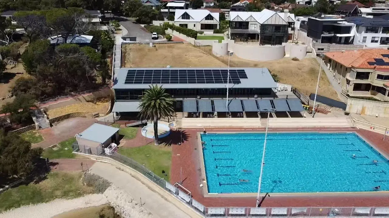 Aerial view of a solar system on a facility beside an outdoor swimming pool