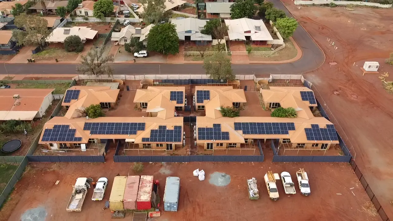 Aerial view of solar panels across the rooftops of a residential village in red-dirt country